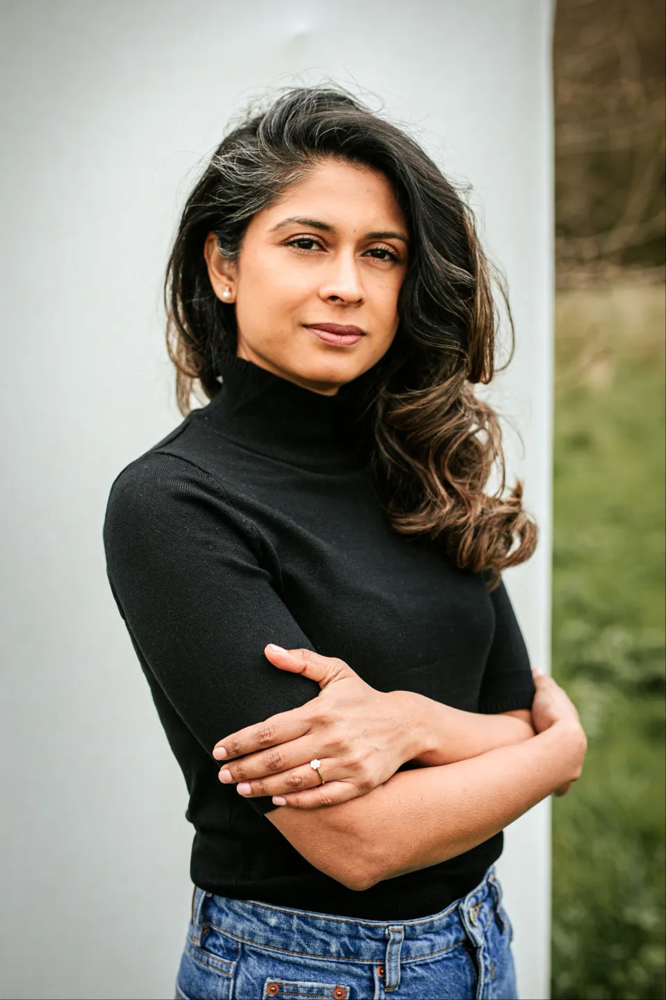 Confident woman in a black turtleneck poses outdoors with arms folded across her chest.
